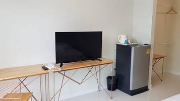 A compact room with a wooden desk, a black TV, a small fridge, and a hanging coat rack.