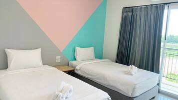 A hotel room with two beds, a small table, a power outlet, and a large window with curtains.
