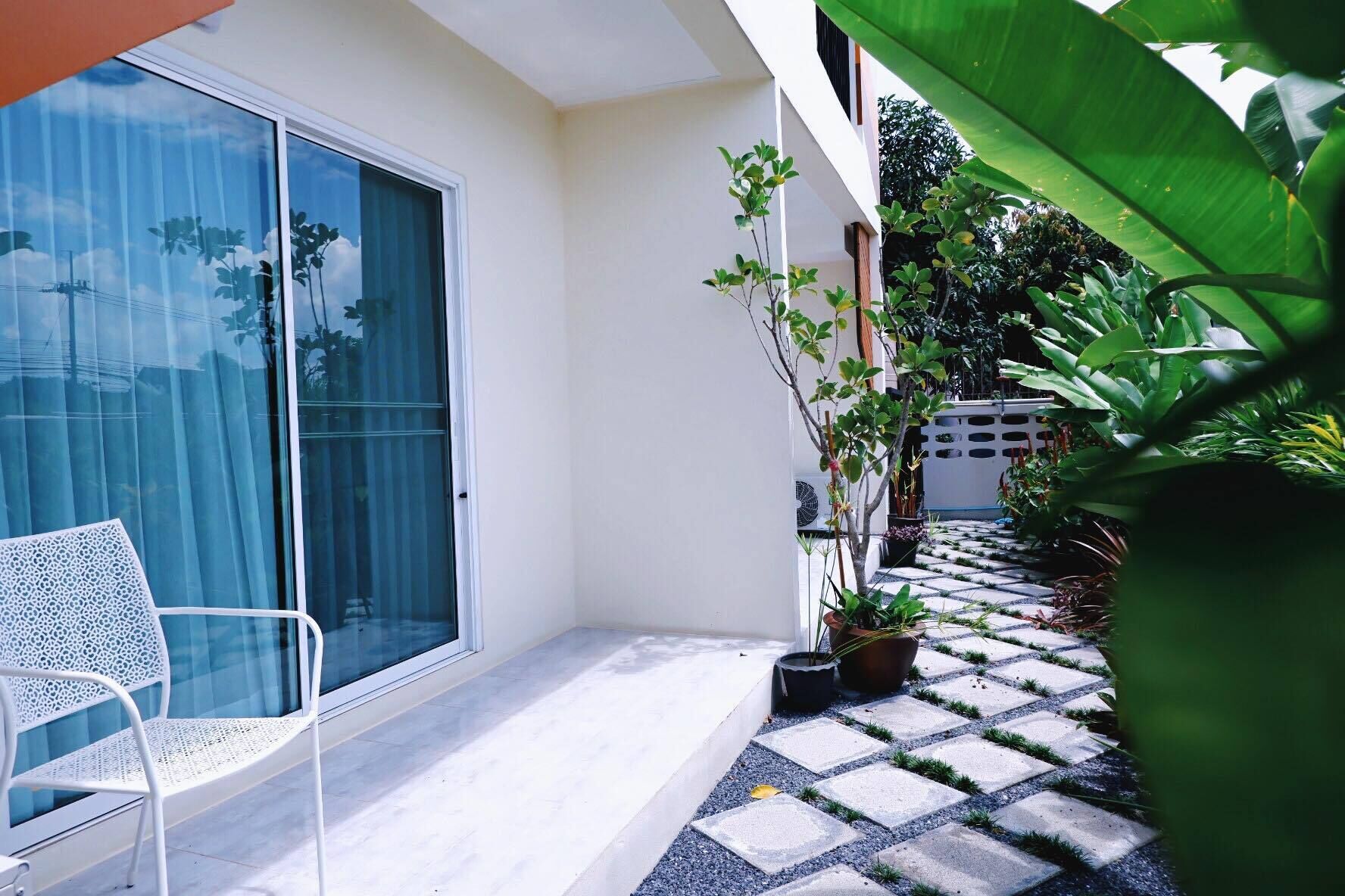 A balcony with a white chair, potted plants, and a tiled pathway.