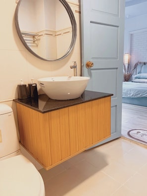 Une salle de bain avec un lavabo blanc, un meuble en bois et un miroir rond.