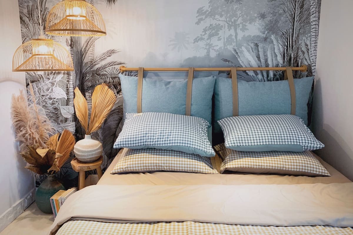 A bedroom with a bed, checkered pillows, a nightstand, a lamp, and a wall mural.