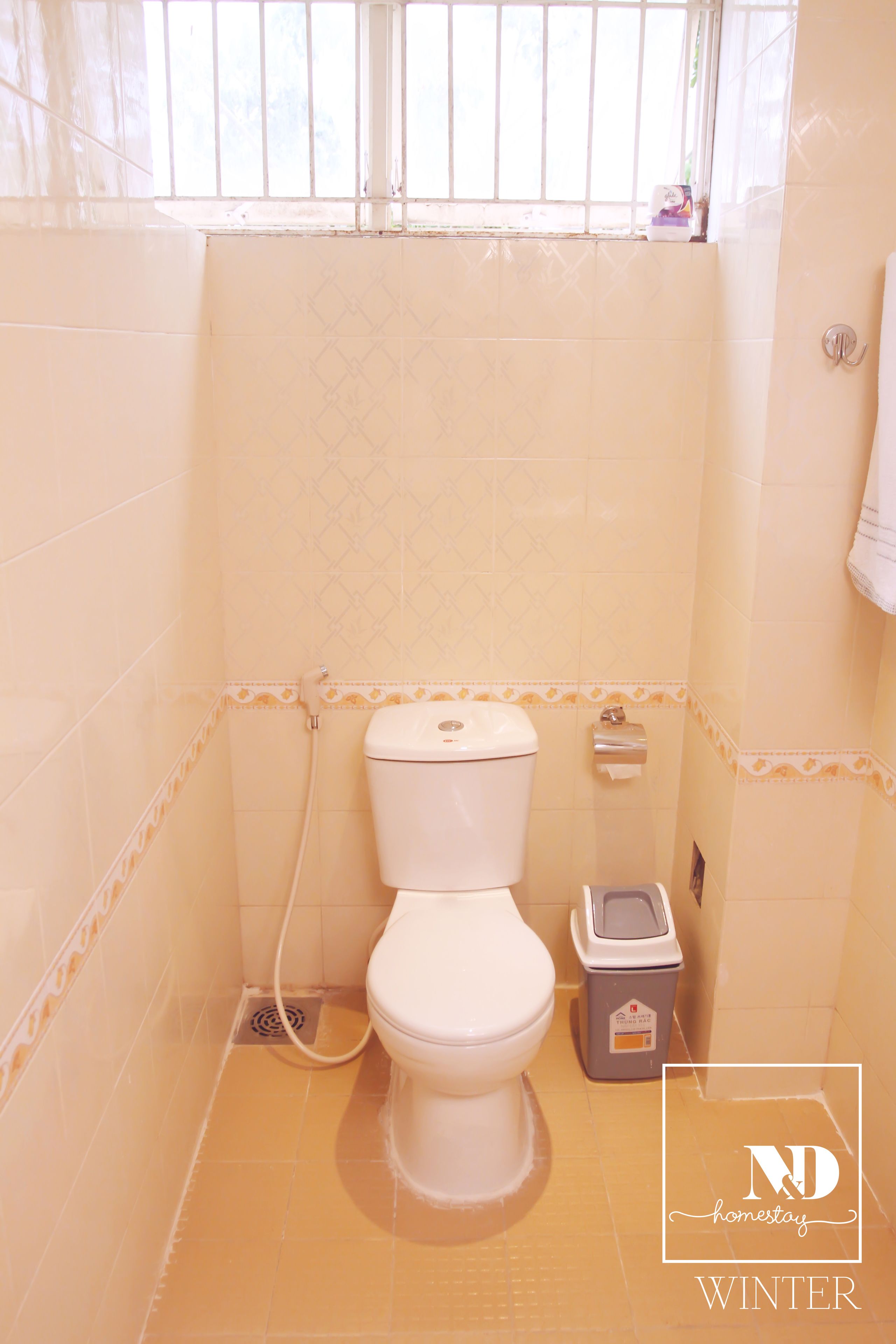 A small bathroom with a toilet, a trash bin, and a window.
