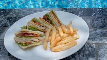 A plate with a sandwich and French fries by a poolside.