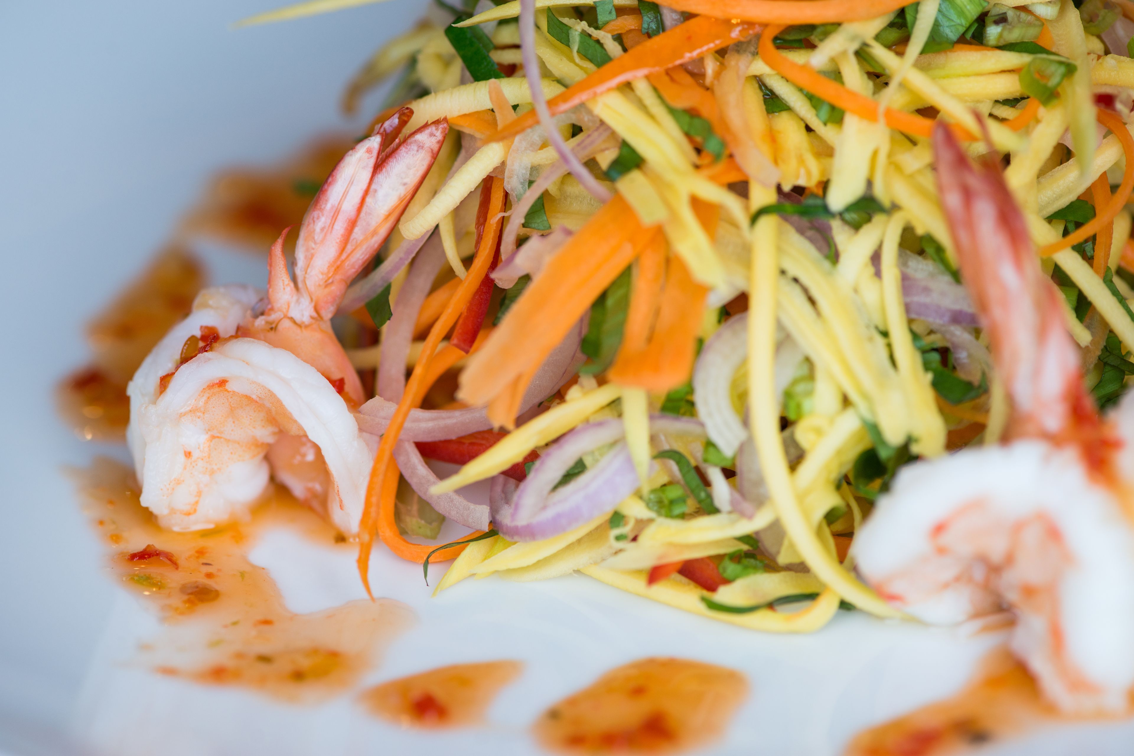A plate of shrimp salad with shredded vegetables and a sauce.