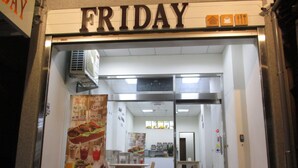 Een restaurantingang met een 'FRIDAY' bord, een menukaart en een zithoek met tafels en stoelen.