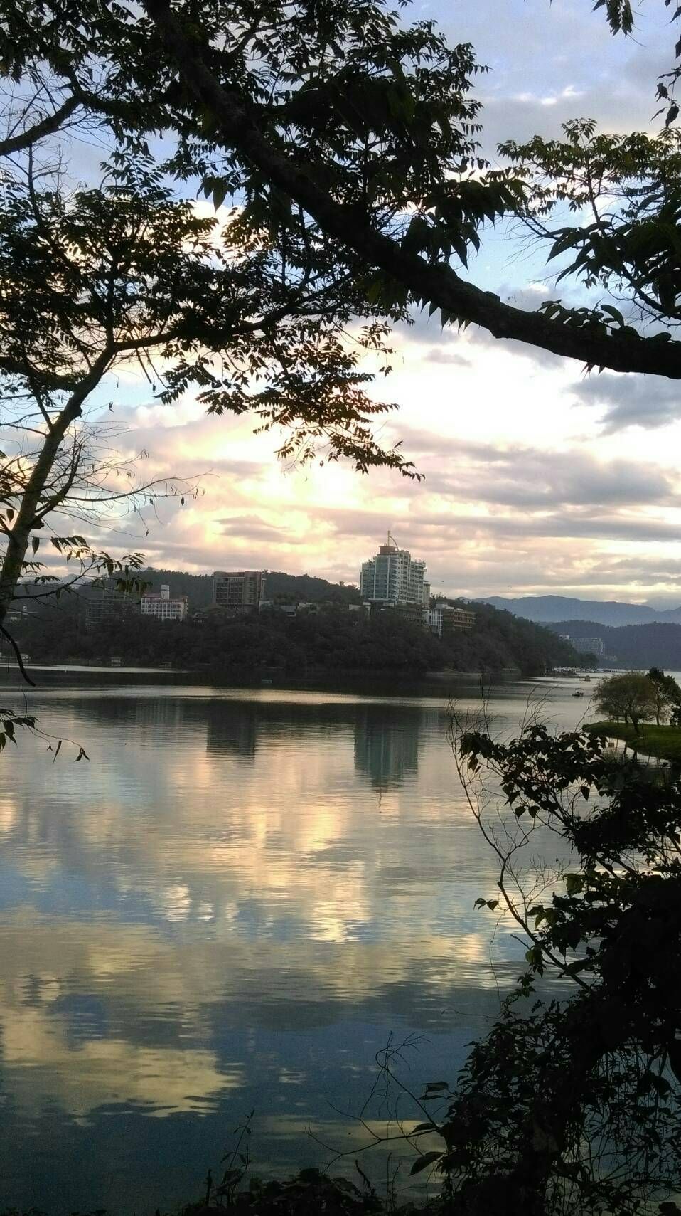 A calm lake with reflections of trees and a cloudy sky.