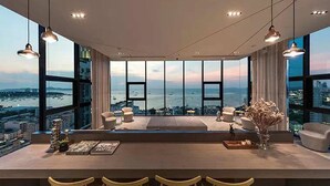 Un espacio moderno para estar con un amplio ventanal que da a una vista de la ciudad y al agua. Hay varias zonas de estar y una barra.