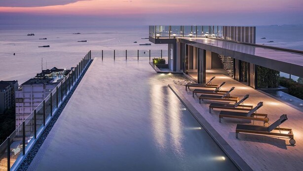 Un hotel frente al mar con una larga terraza abierta que da al océano, con tumbonas y barandilla de cristal.