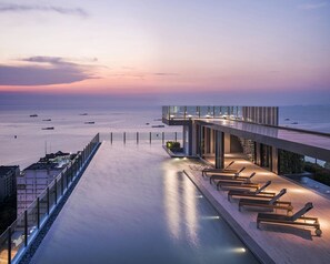 Un hôtel situé au bord de l’eau, doté d’une longue terrasse ouverte donnant sur la mer, avec des chaises longues et une balustrade en verre.