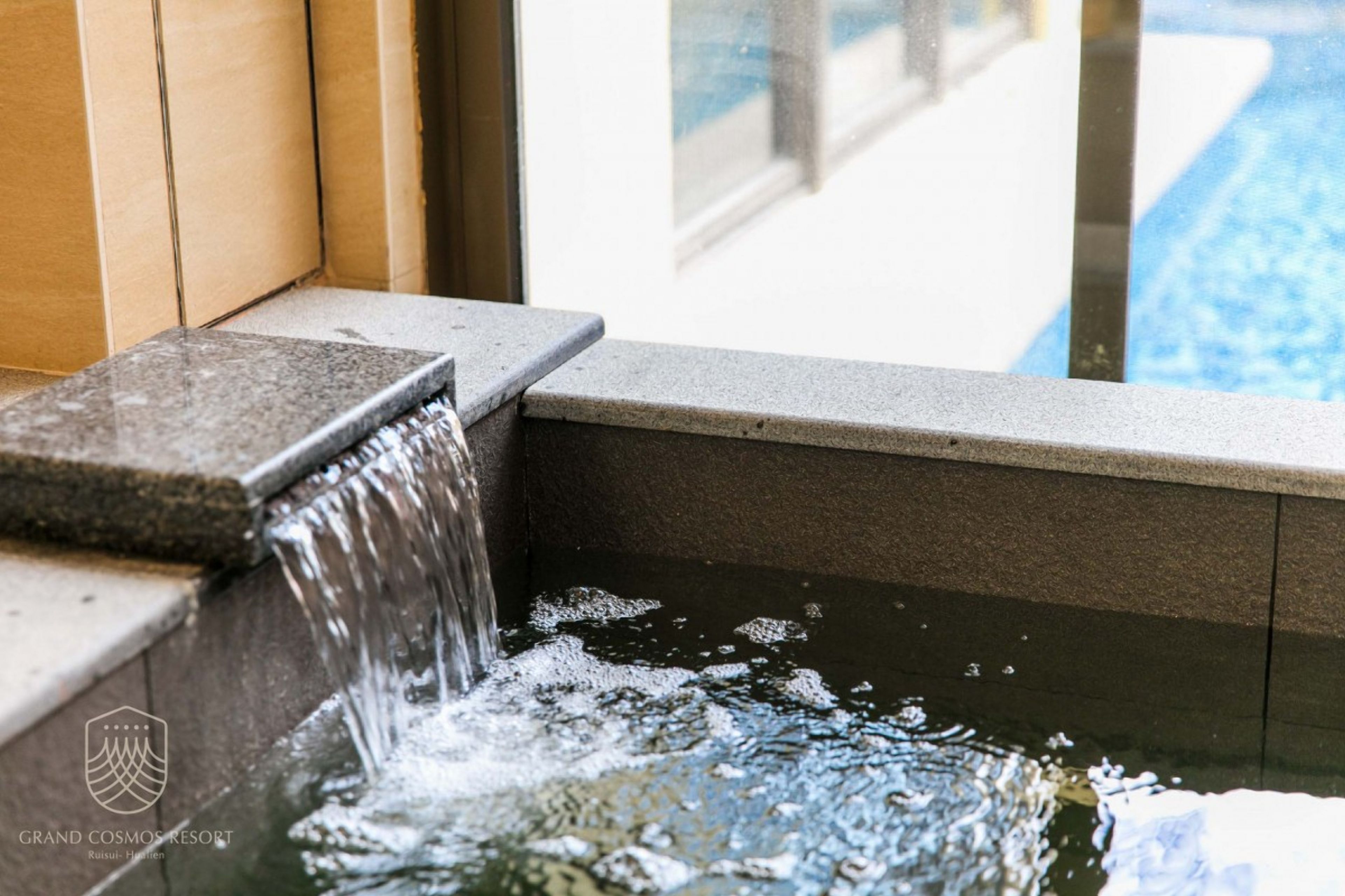 Una fuente de agua con un borde de piedra y una piscina al fondo.