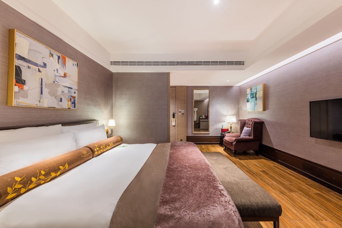 A hotel room with a large bed, a bench, a seating area, a TV, and artwork on the walls.