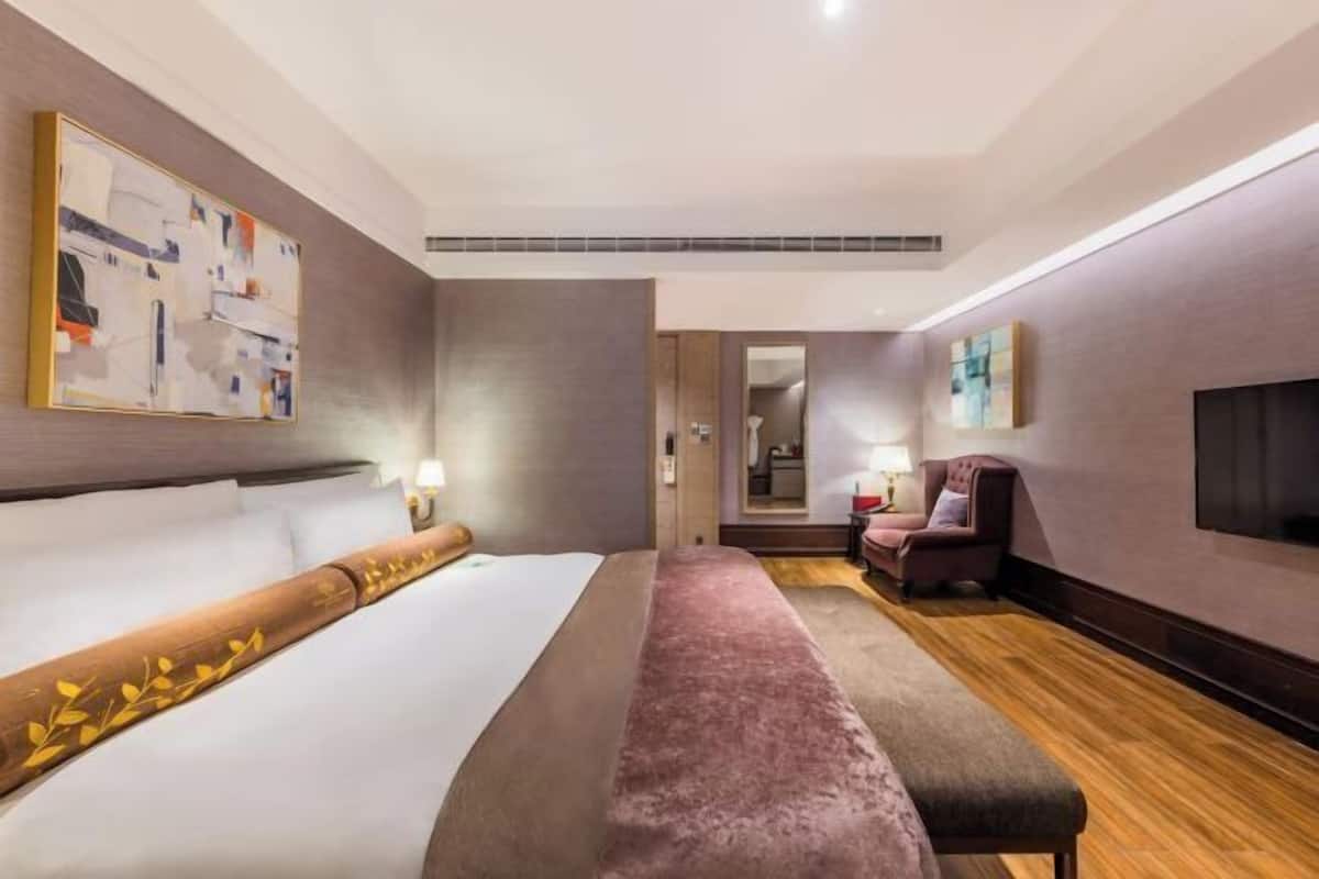 A hotel room with a large bed, a bench, a TV, and a bathroom visible through a door.