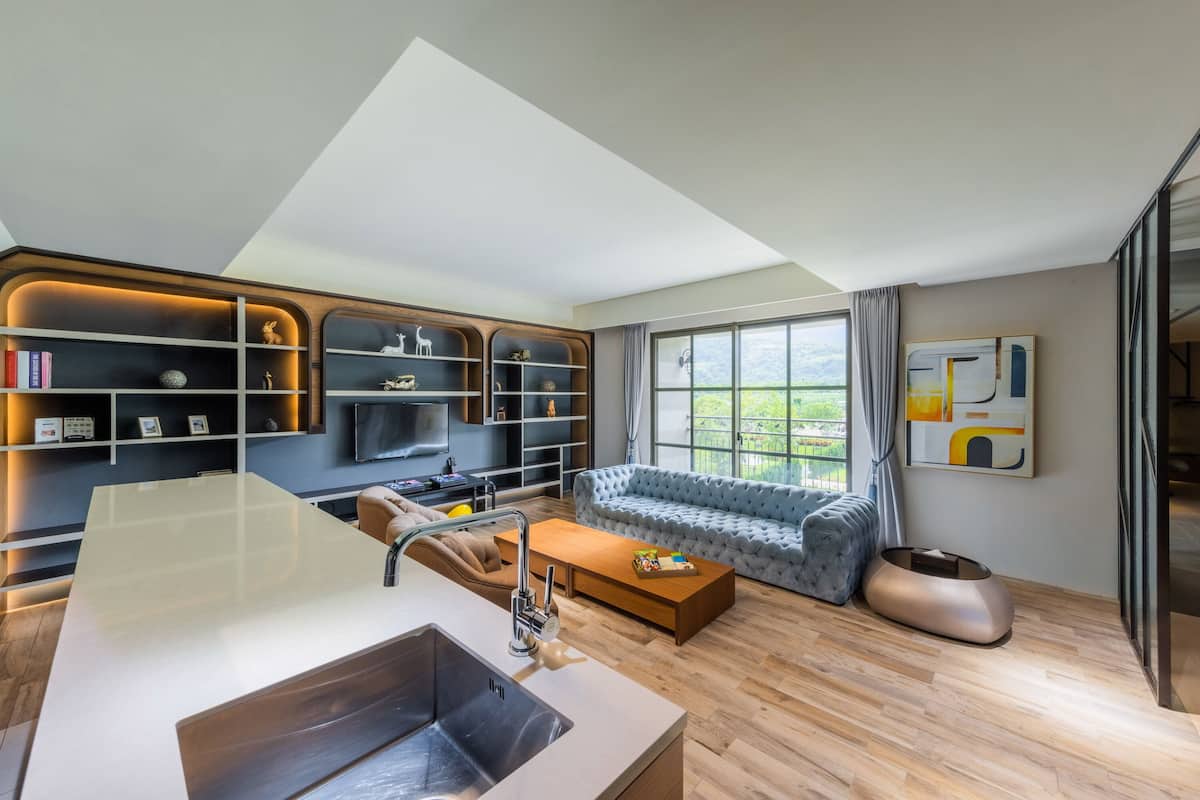 A modern living room with a large window, a sofa, a coffee table, and a built-in bookshelf.