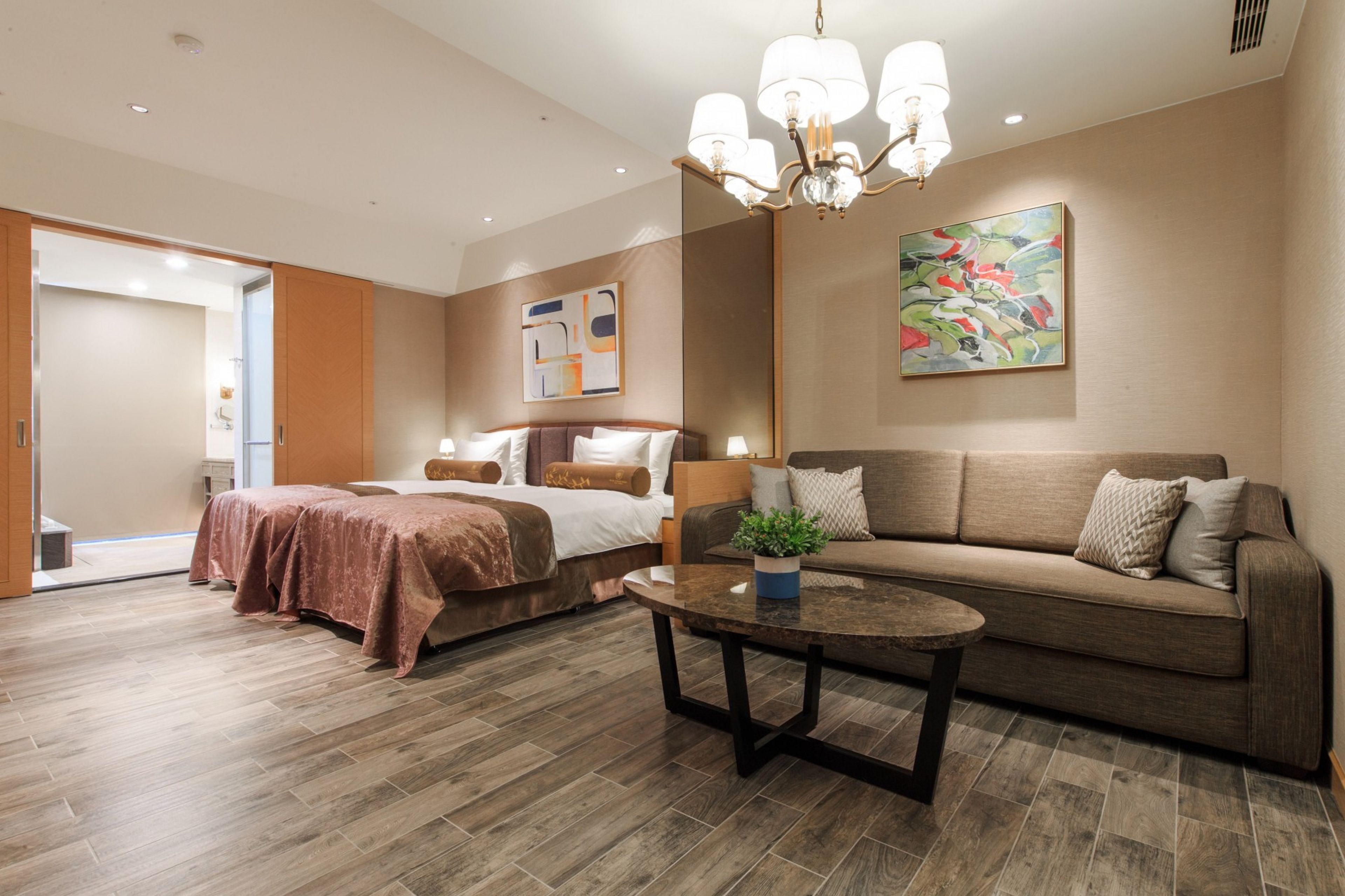 A modern hotel room with a bed, a sofa, a coffee table, and a chandelier.