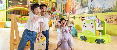 Espaço infantil com casinha de madeira, cadeira em formato de sapo verde e painel decorativo com pássaro e peixe.