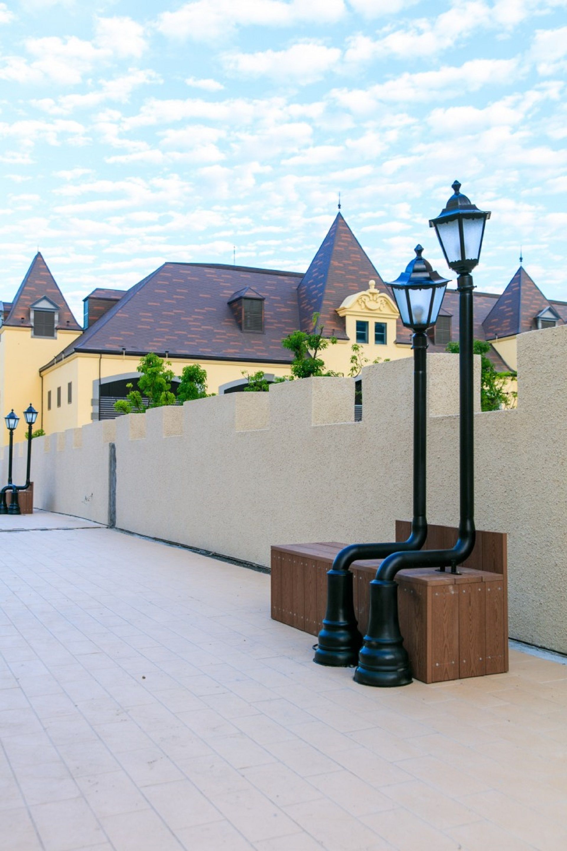 Un sendero adoquinado con un farol y bancos, rodeado por un muro bajo y edificios con características arquitectónicas destacadas.