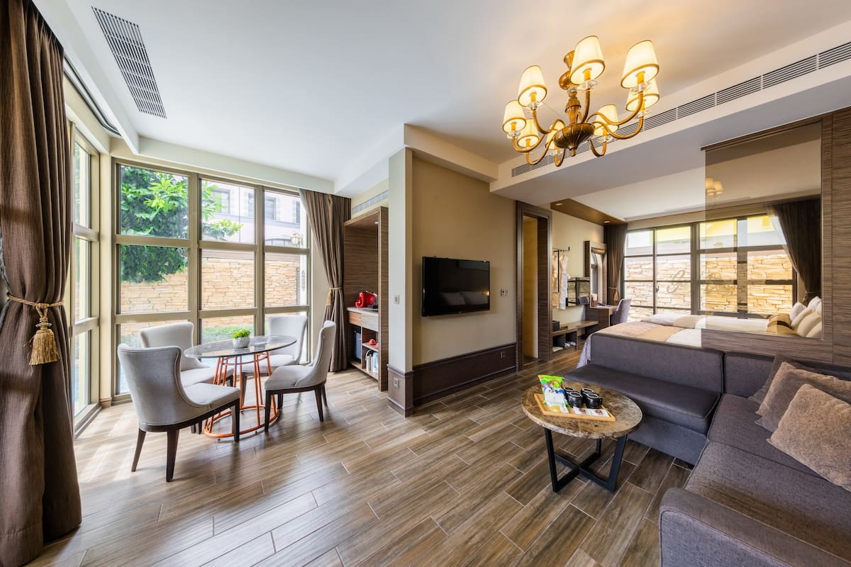 A spacious living room with a large sofa, a dining area with chairs, a coffee table, and a TV mounted on the wall.