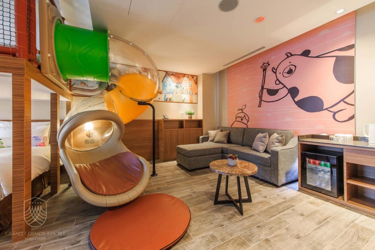 A modern hotel room with a curved seating area, a sofa, a small table, and a refrigerator.
