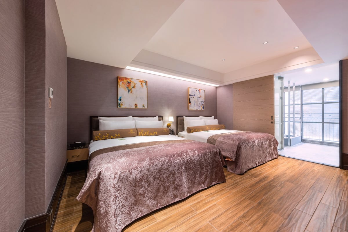 A modern hotel room with two beds, a large window, and artwork on the walls.