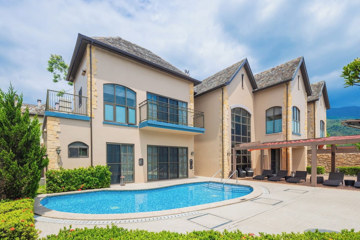 A two-story house with a swimming pool, outdoor seating, and a stone facade.