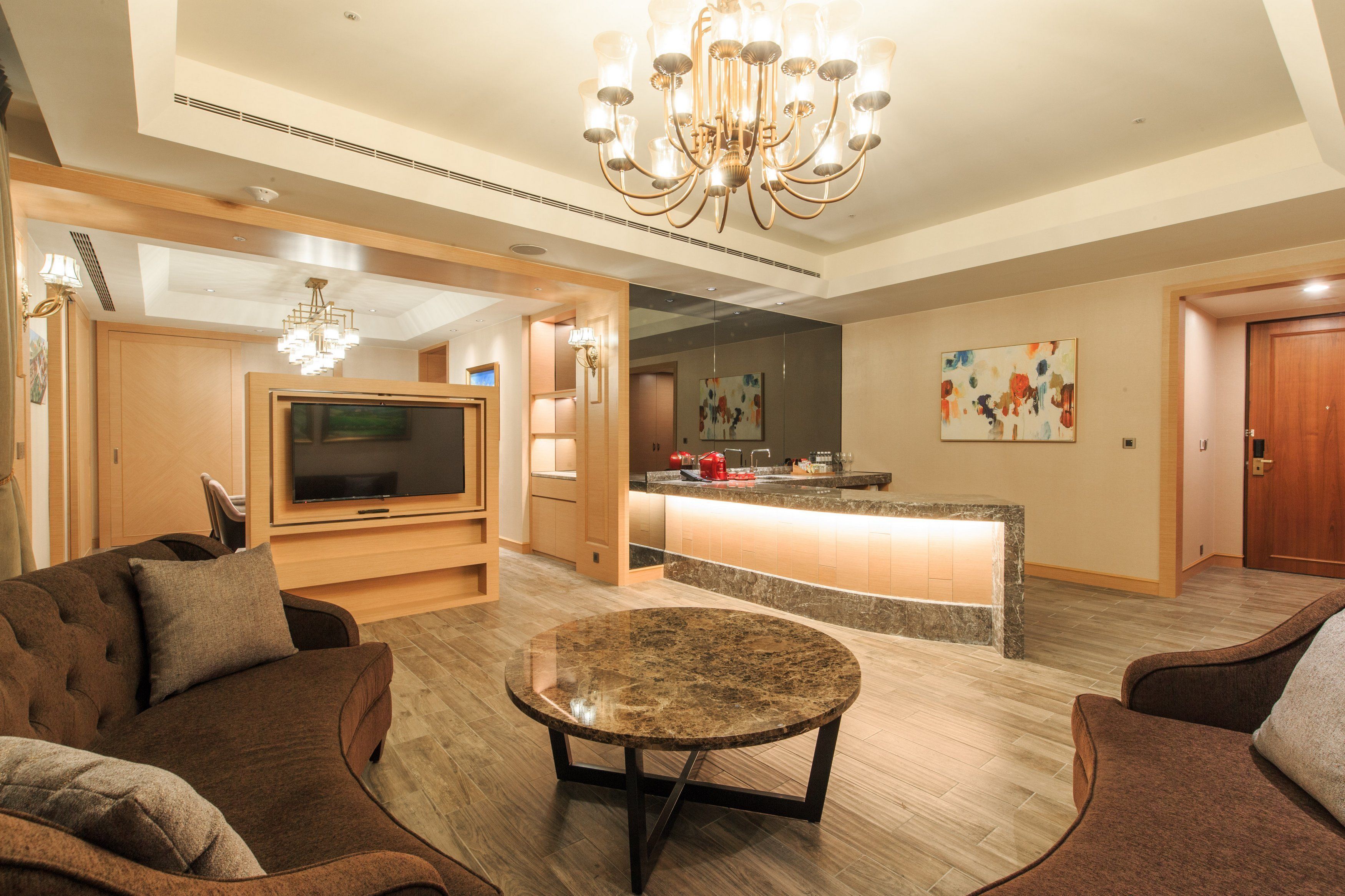 A modern living room with a TV, a round coffee table, and a chandelier.