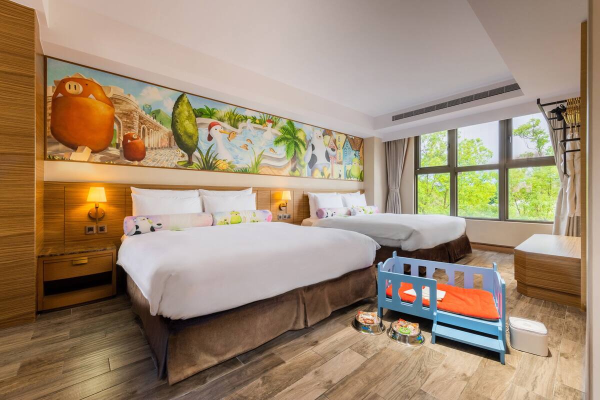 A hotel room with two beds, a mural, and a view of greenery.