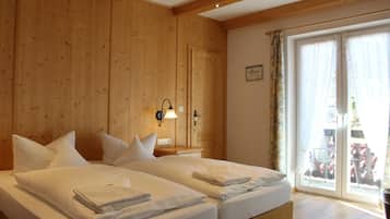 Une chambre double aux murs en bois, avec une grande porte-fenêtre coulissante sur le côté droit, et deux lits avec du linge de lit blanc.