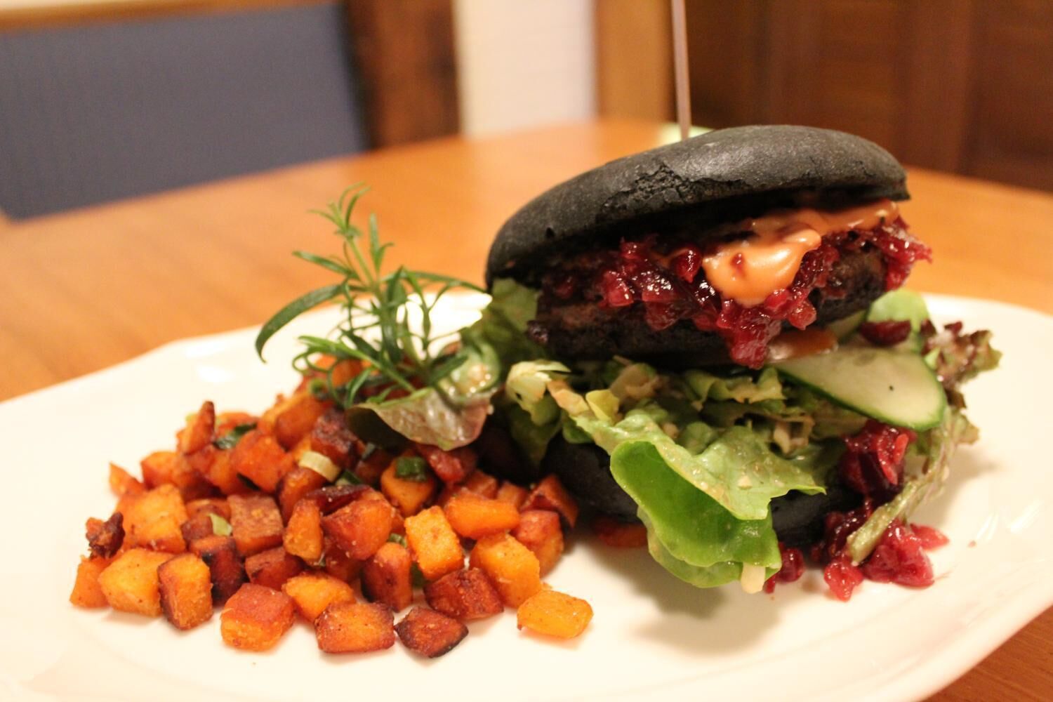 Hamburguesa con pan negro, cubierta de salsa roja, lechuga y una rebanada de queso, acompañada de una guarnición de papas al horno.