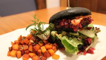 Hamburguesa con pan negro, cubierta de salsa roja, lechuga y una rebanada de queso, acompañada de una guarnición de papas al horno.