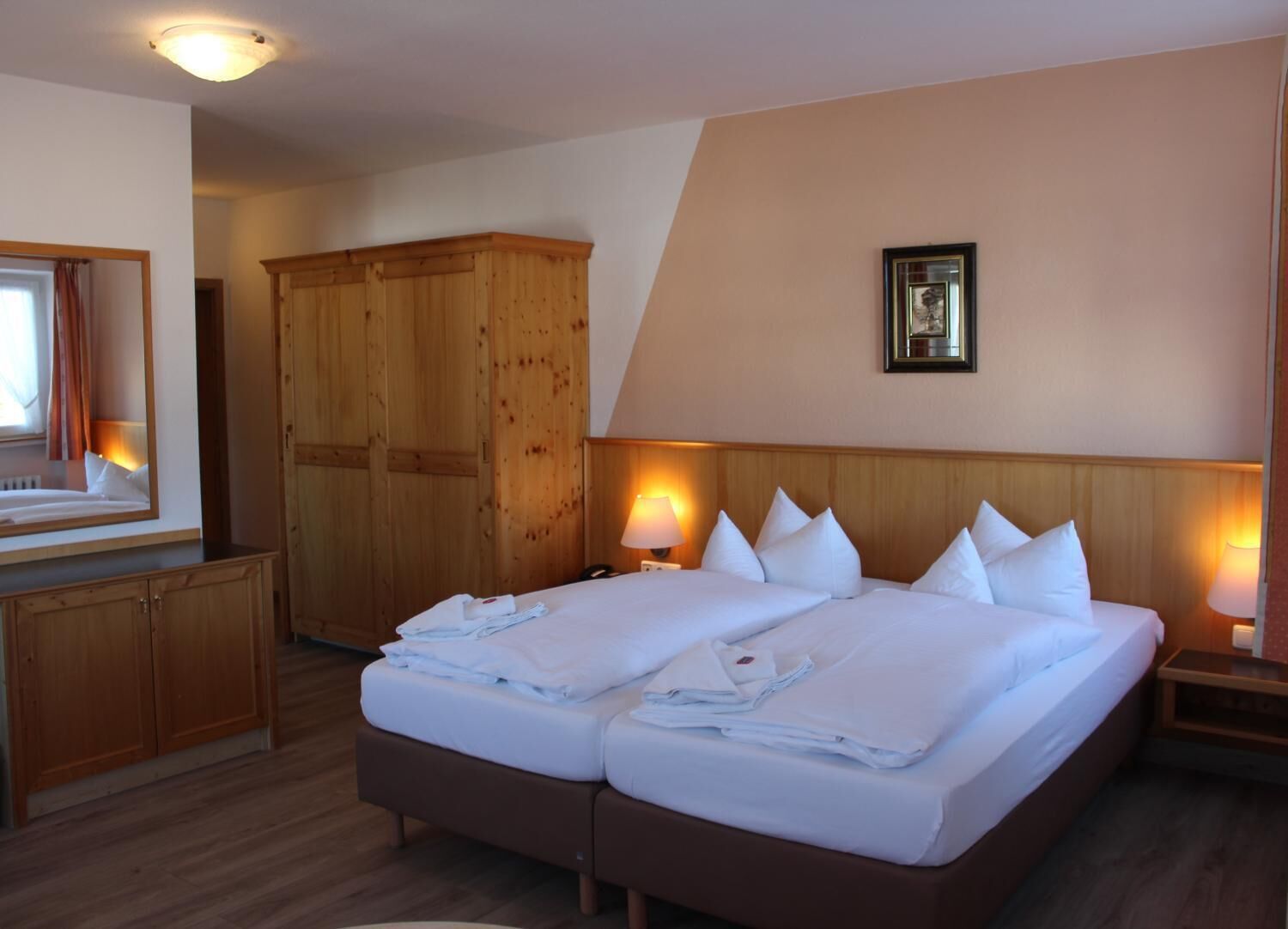 A hotel room with a large bed, wooden wardrobe, and a mirror.