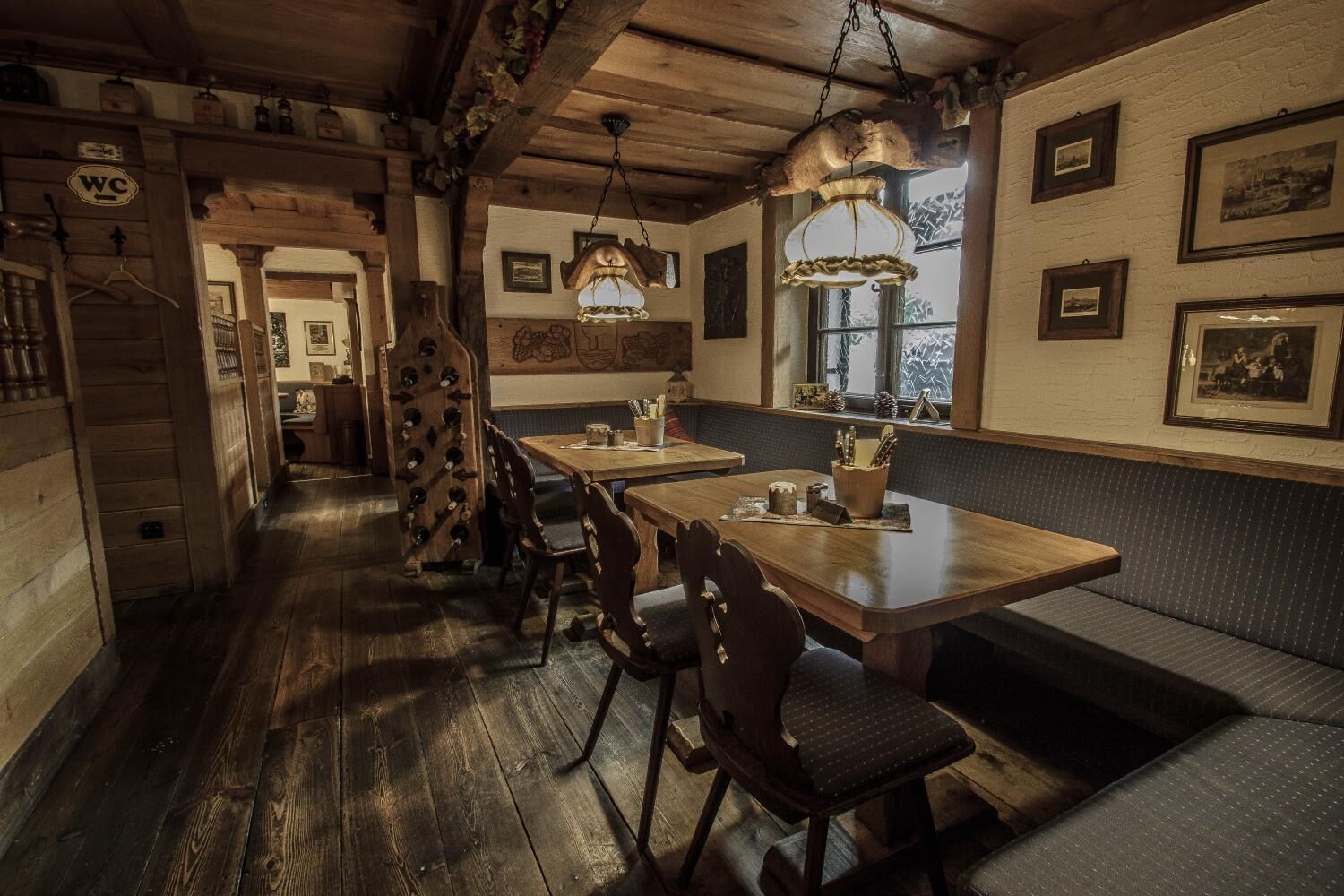 A rustic wooden interior with a long table and benches, wooden ceiling beams, and framed pictures on the walls.