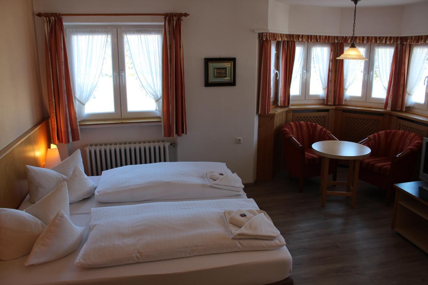 A hotel room with two beds, a dining area with a table and chairs, and a radiator.