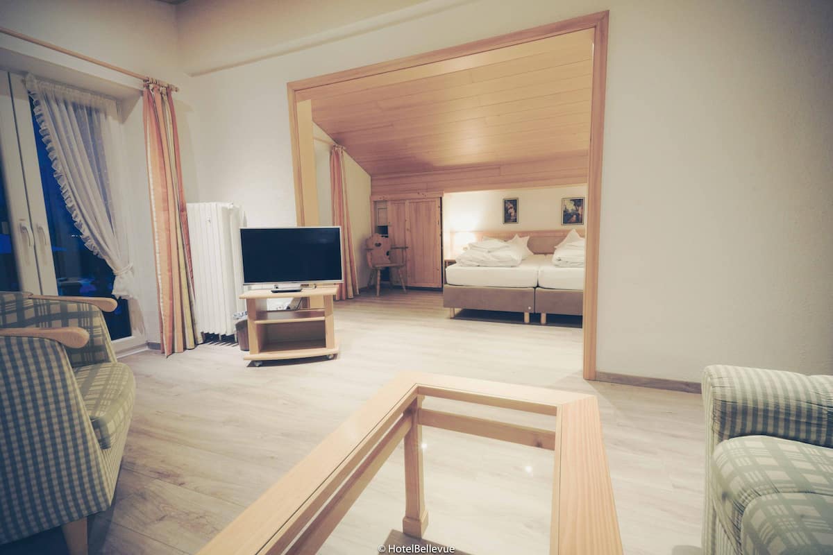 A hotel room with a wooden ceiling, a bed, a TV, and a seating area with a table and chairs.