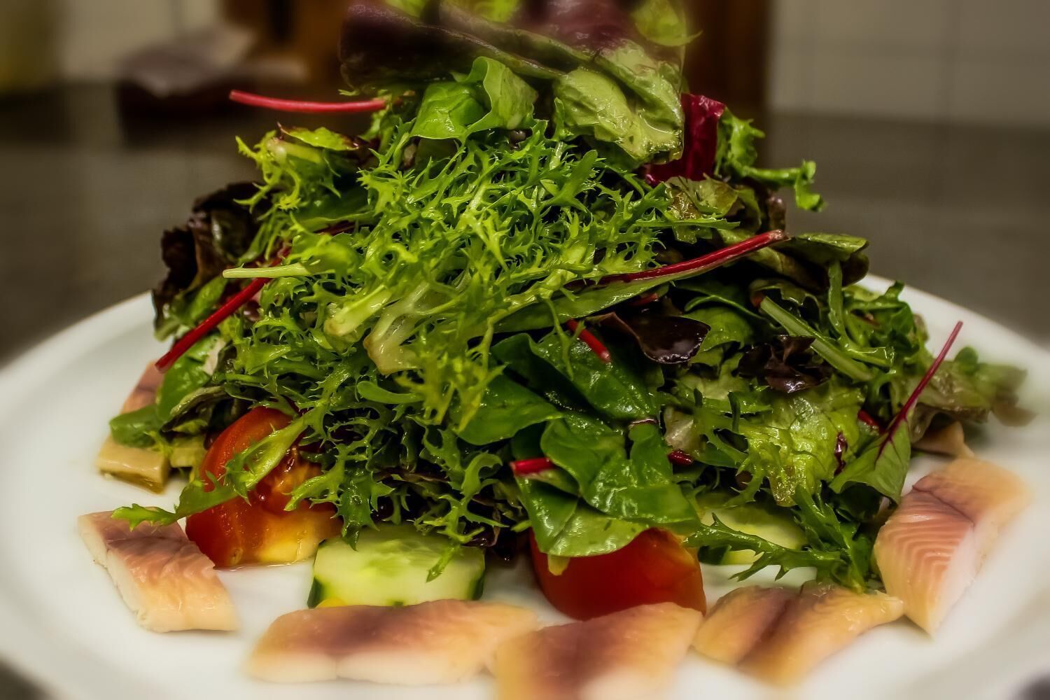 Ensalada de hojas verdes variadas con tomates y rodajas de pepino.