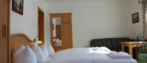 Ein Hotelzimmer mit einem großen Bett, einem Holz-Kopfteil, einem Spiegel, einer grünen Couch, einem kleinen Tisch und einem blumigen Vorhang.