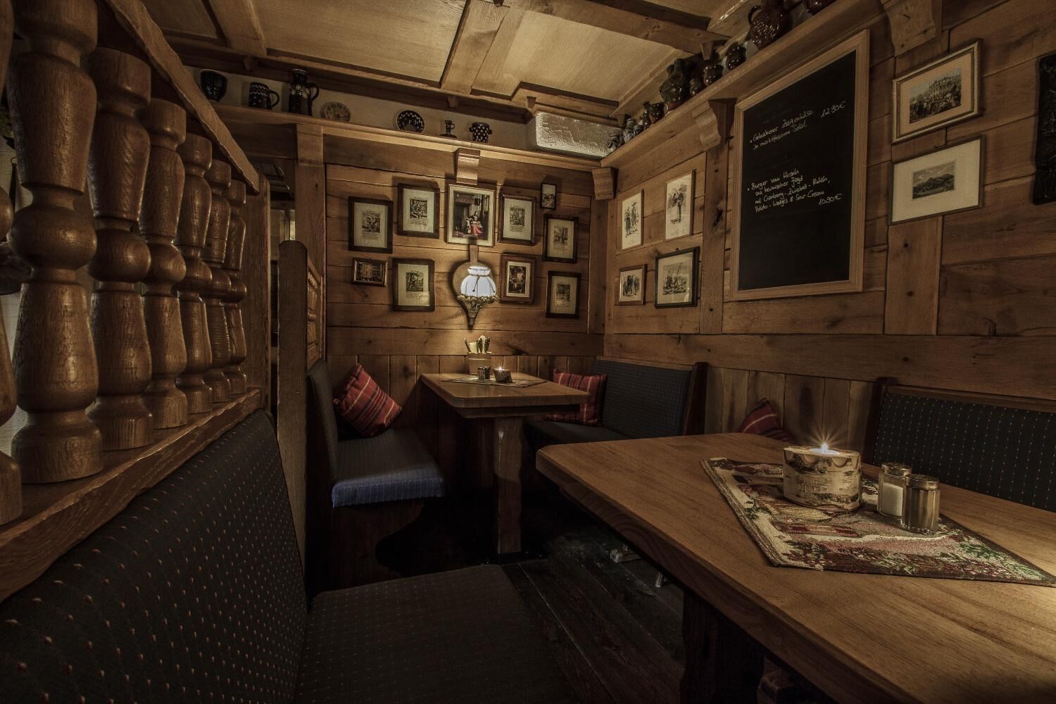 A cozy restaurant interior with wooden walls, framed pictures, and a chalkboard menu.