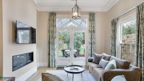 A living room with a sofa, a coffee table, a flat-screen TV, and a large window with curtains. - Grandview Accommodation - The Elm Tree Apartments (Mount Barker)