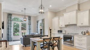 A modern kitchen with white cabinets, a built-in oven, and a dining area with a wooden table and chairs. - Grandview Accommodation - The Elm Tree Apartments (Mount Barker)