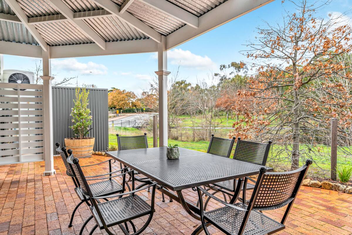 An outdoor patio with a metal table and chairs, a potted plant, and a view of the surrounding landscape.