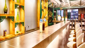 A bar area with a long counter, shelves with decorative items, and seating with cushioned chairs. - The Herb Farm (Igatpuri)