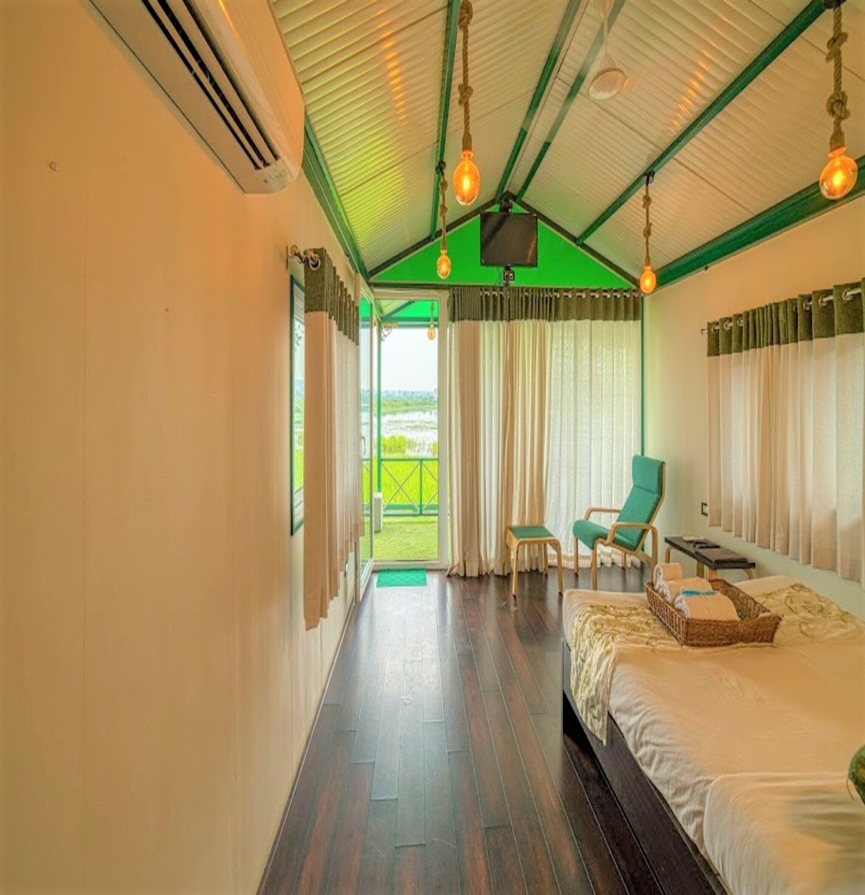 Quarto com cama, duas cadeiras, televisão e vista para o exterior.