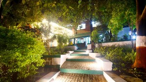 A nighttime outdoor staircase leading to a building with a traditional architectural style, surrounded by lush greenery. - The Herb Farm (Igatpuri)