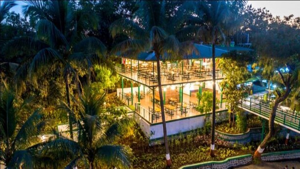 A multi-level building with outdoor seating areas surrounded by palm trees. - The Herb Farm (Igatpuri)