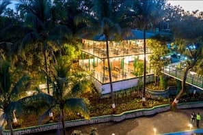 A multi-level building with outdoor seating areas surrounded by palm trees. - The Herb Farm (Igatpuri)
