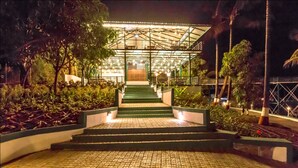 A nighttime view of a building with a glass facade and a staircase leading to a covered entrance. - The Herb Farm (Igatpuri)