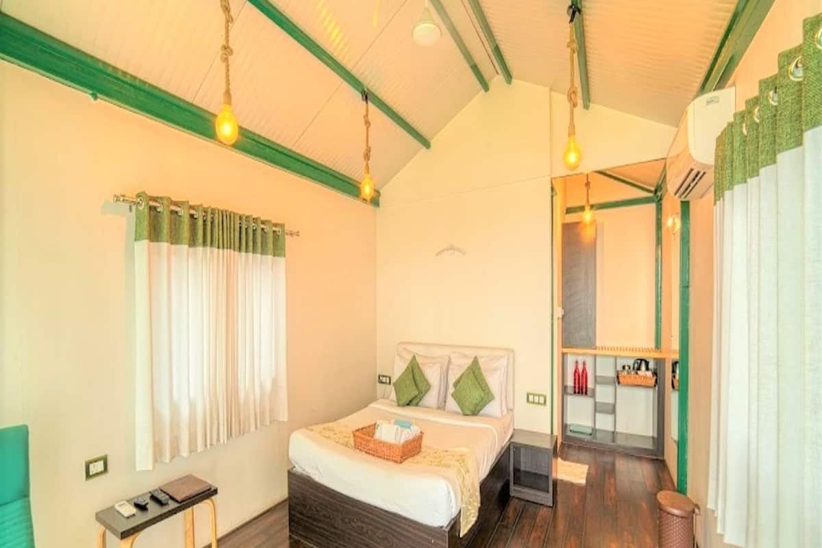 Habitación de hotel con piso de madera, cama con almohadas, una mesita y una silla. Se ve un baño a través de una puerta abierta.