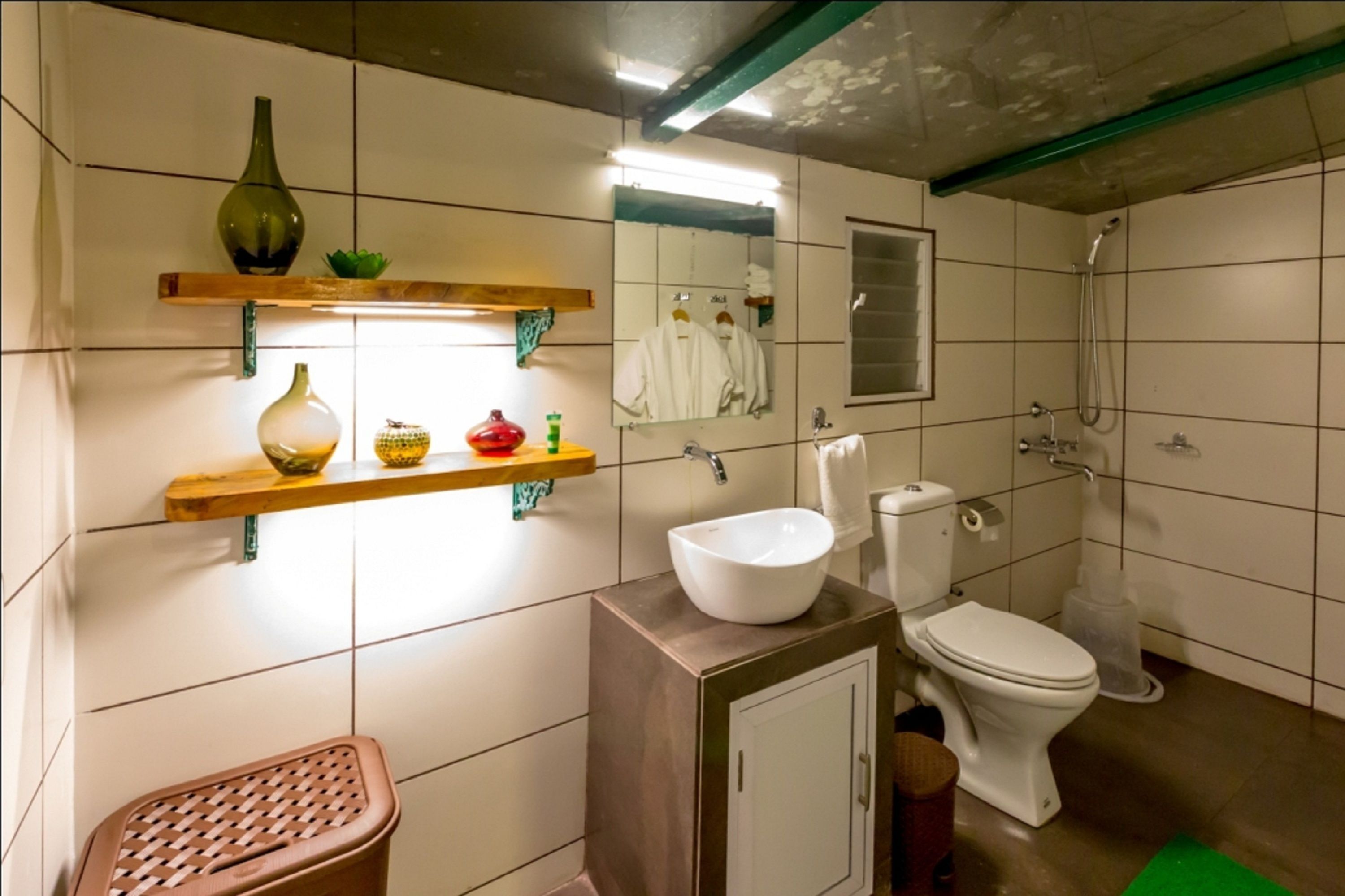 Un baño con inodoro, lavamanos, espejo, ducha y repisas con objetos decorativos.