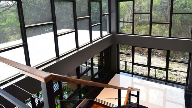 Un interior moderno con ventanas amplias, una escalera de madera y una lámpara colgante.