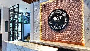 Un área de recepción con mostrador de mármol, pared con diseño geométrico y un letrero circular que dice "The Nest Hotel by Play".