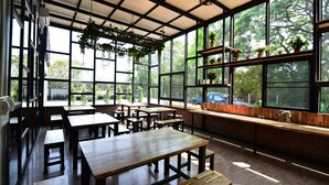Un espacio interior amplio con grandes ventanales, mesas y bancos de madera, y plantas colgantes.